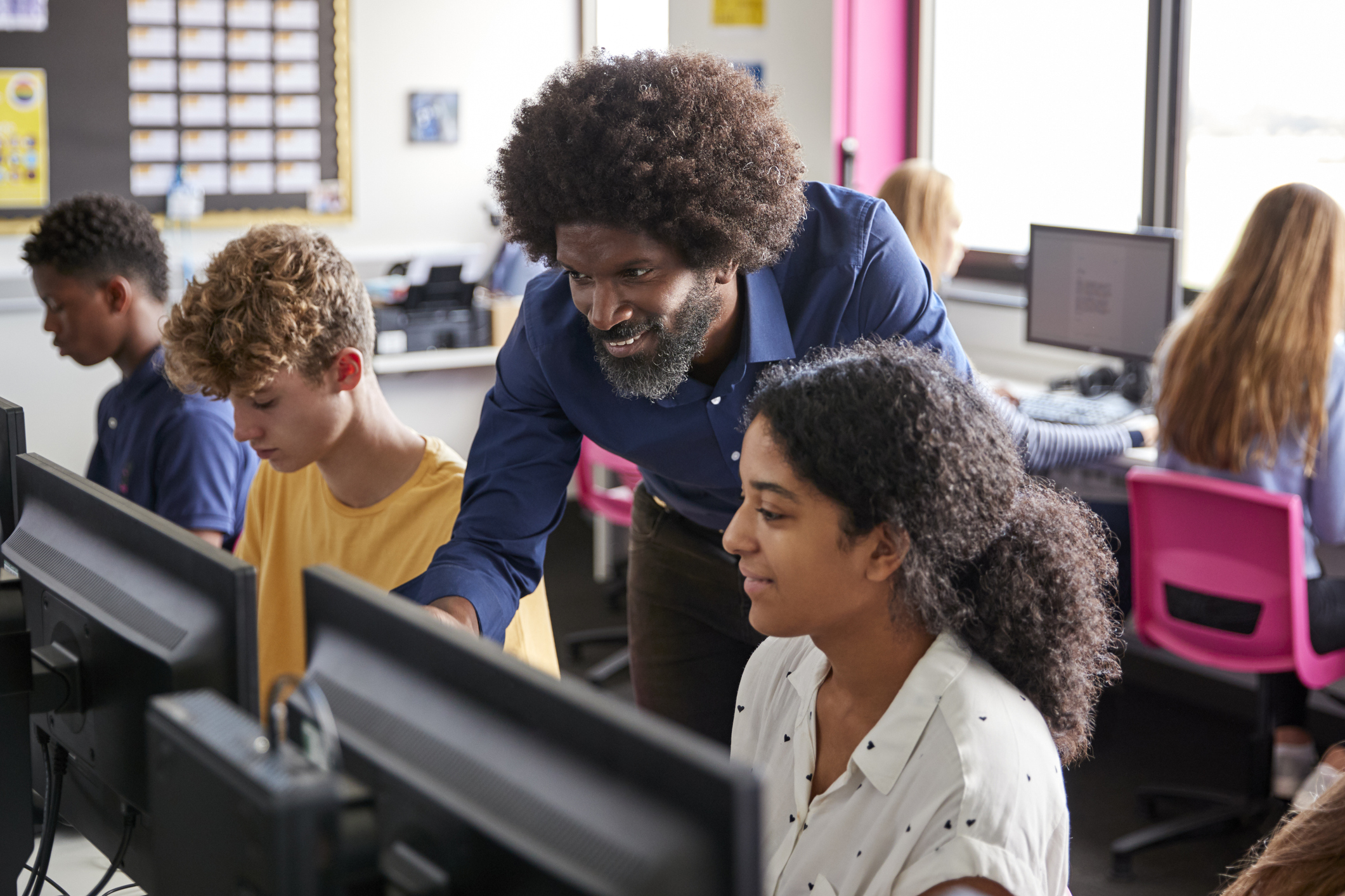 male teacher helping teenage students in computer class